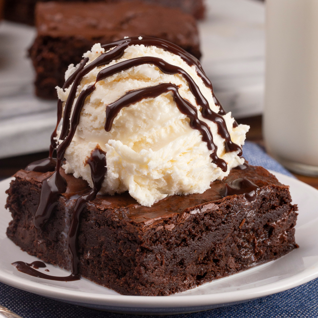 Brownie with vanilla ice cream and chocolate drizzle on a white plate. Indulge your sweet side with our plant-based desserts — from gooey brownies to homely apple pie — the perfect end to a nourishing day.